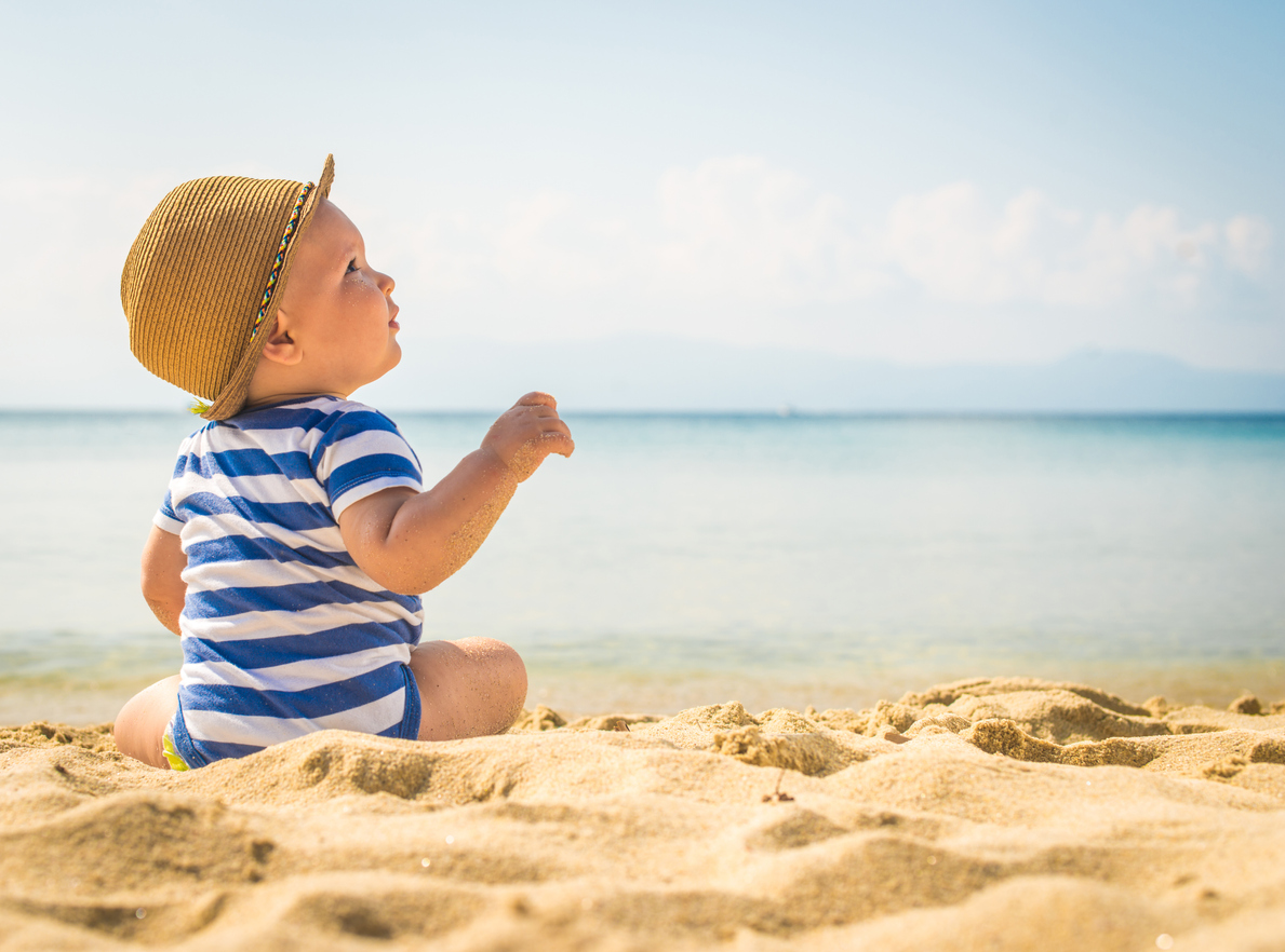 The cute baby boy playing on the beach. Little boy sitting on the sand. Sea and seashore as background with copy space