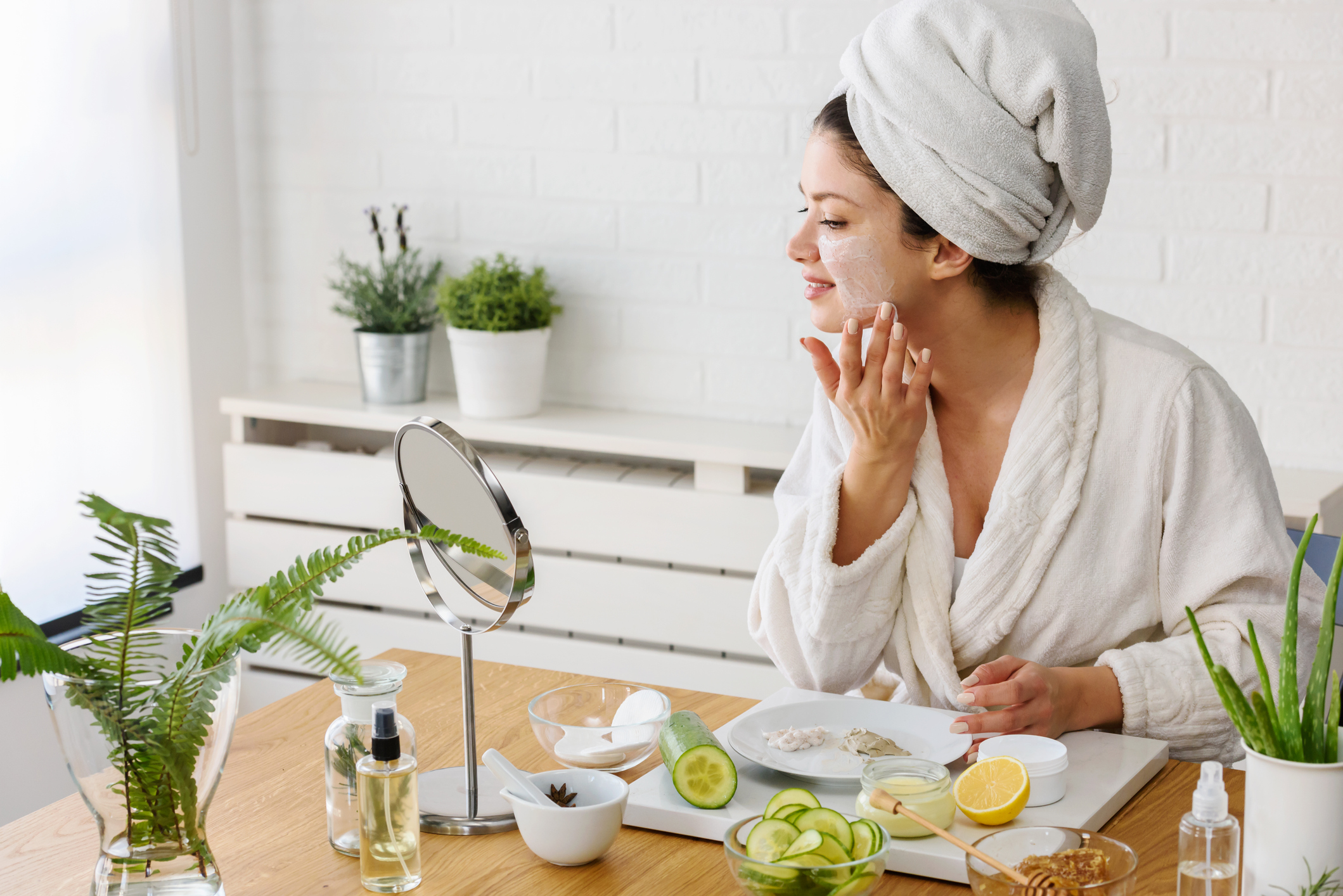 Young woman cleaning face with natural cosmetics. How to get clear and glowing skin. Portrait of young woman with clay face mask on wearing bathrobe. Homemade Face Mask
