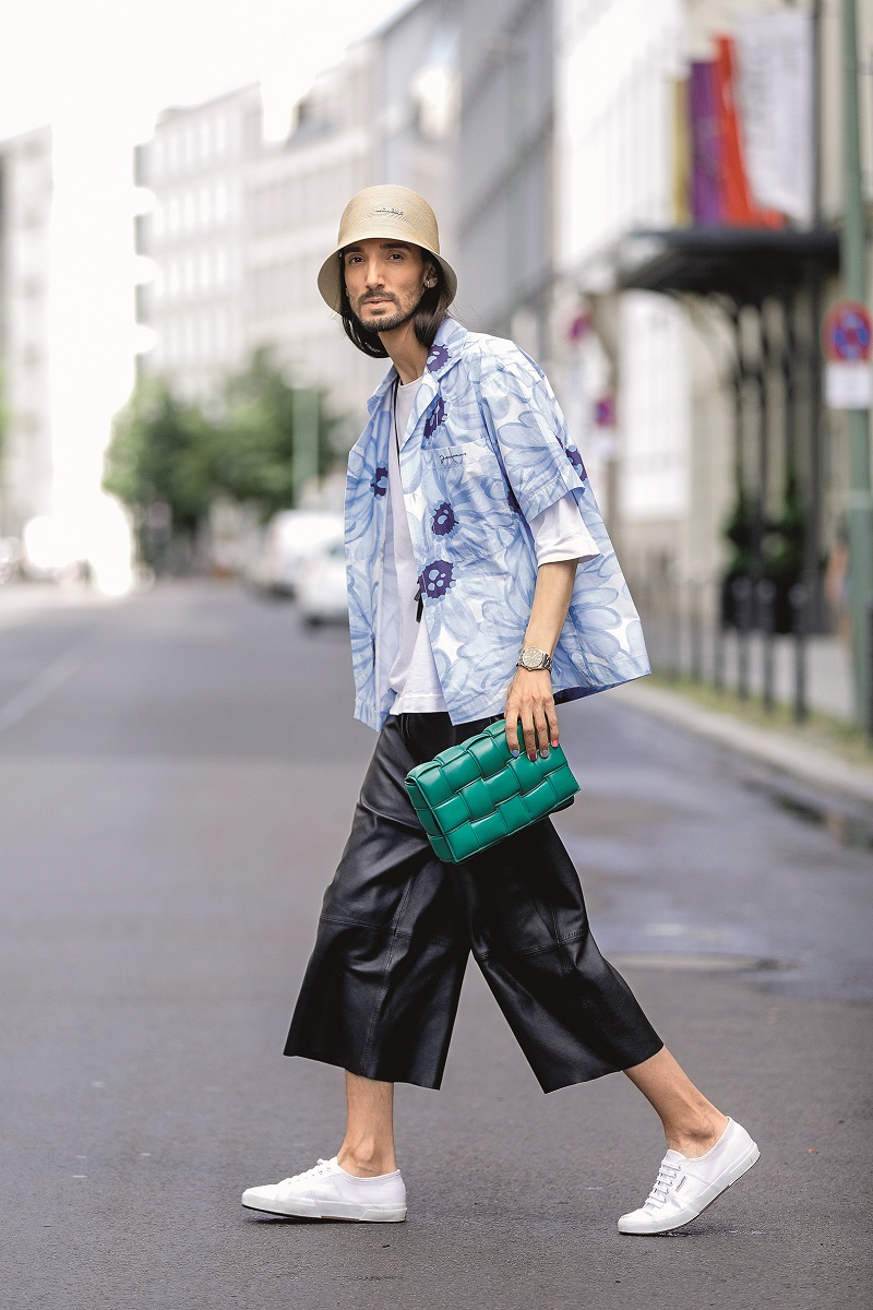 BERLIN, GERMANY - JULY 22: Trend scout Julian Daynov, wearing a beige cap by Jacquemus, a white t-shirt by Jil Sander, a blue printed shirt by Jacquemus, black pants by Joseph, white sneakers by Superga, a mini chain bag by Jacquemus and a green padded cassette bag by Bottega Veneta during a street style shooting on July 22, 2020 in Berlin, Germany. (Photo by Streetstyleograph/Getty Images)