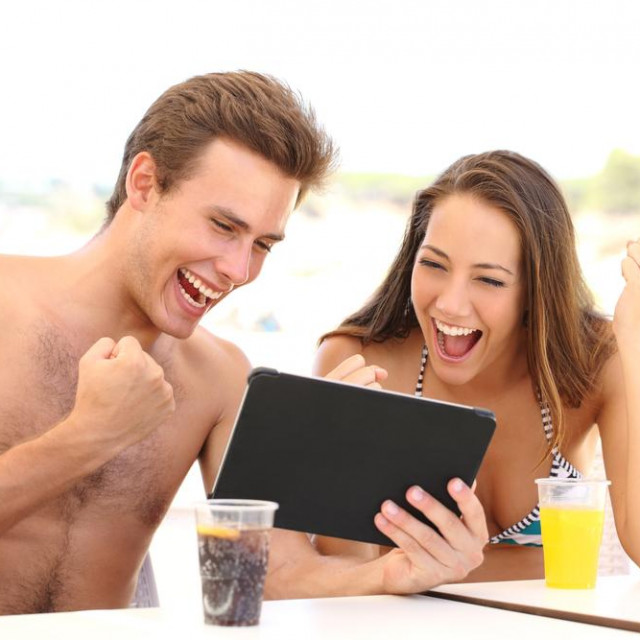 Euphoric couple of winners watching a tablet on the beach in holidays