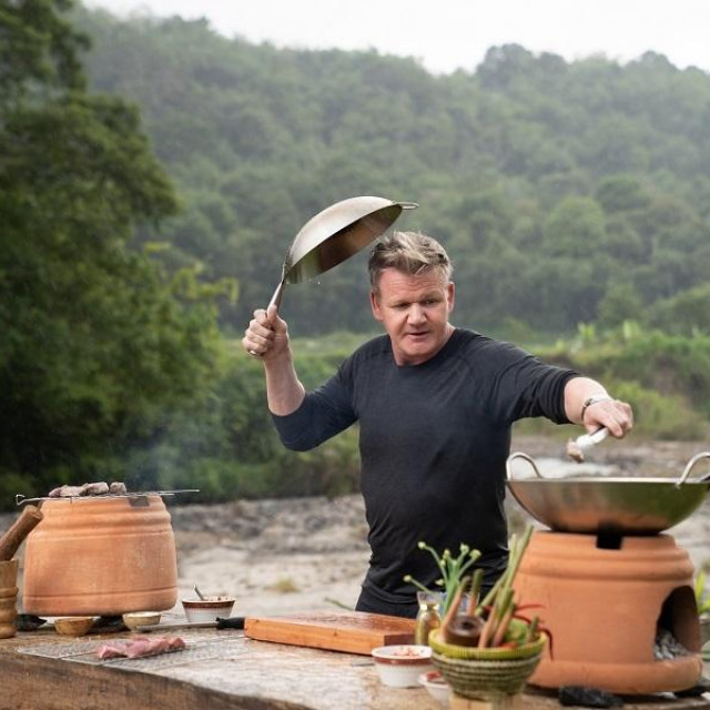 West Sumatra, Indonesia - Gordon Ramsay covers his head with a pot during a quick rain shower while he cooks beef rendang. (National Geographic/Justin Mandel)