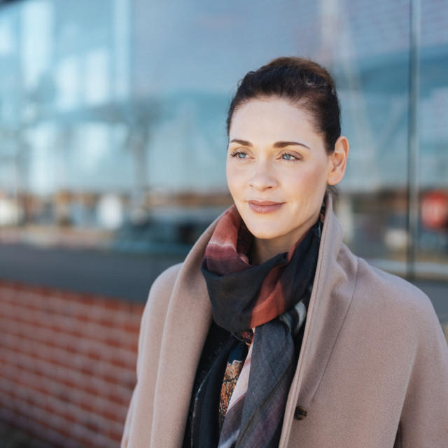 Thoughtful stylish woman with a faraway expression standing in front of a commercial building in town