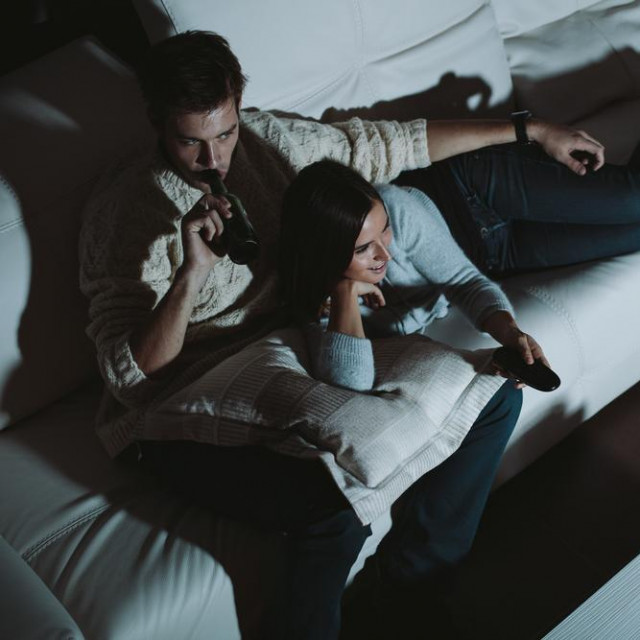 Young couple watching TV at home at night