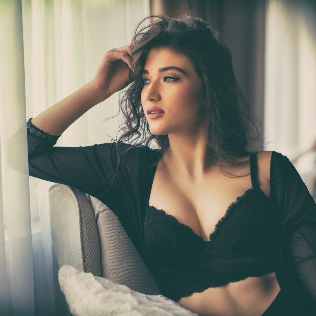 Sensual young woman sitting on chair next to the window and looking away. She wearing black underwear and looks beautiful
