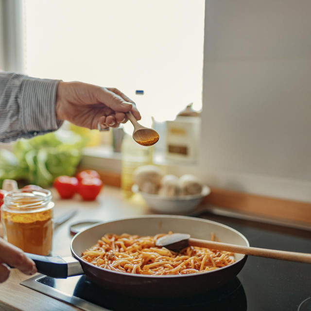 Cropped Image of Woman Hand Adding Turmeric Spice Over a Pan in Her Kitchen While Preparing Lunch. Food, Eating, Culinary and People Concept