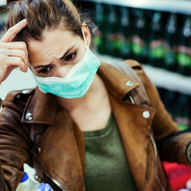 Young woman with face mask thinking and feeling worried while buying in the store during virus pandemic.