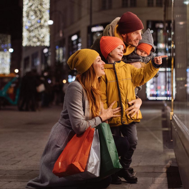 Family with two kids in front of the store window in a big city at night