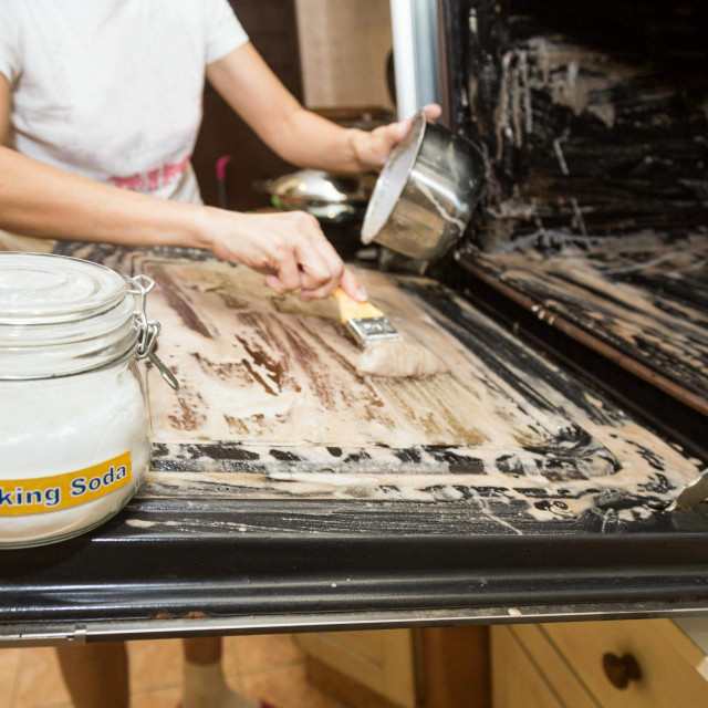 Person applying mixed baking soda onto surface of oven for effective and safe cleaning