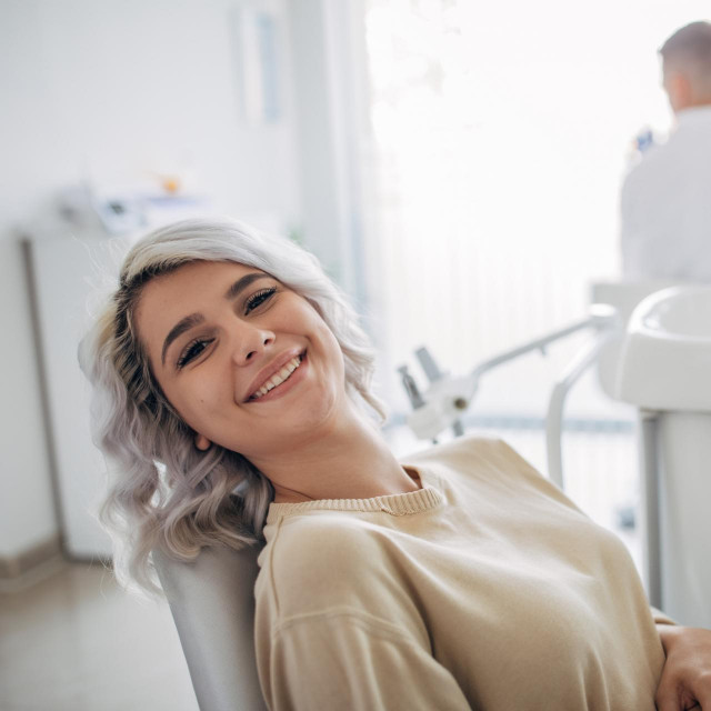 Satisfied dentist patient showing her perfect smile after treatment in a clinic box with medical equipment in the background