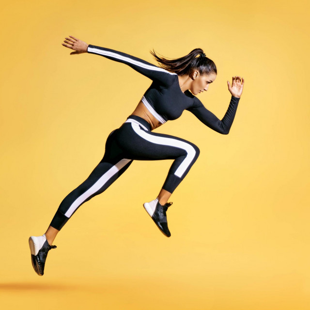 Sporty woman runner in silhouette on yellow background. Photo of attractive woman in fashionable sportswear. Dynamic movement. Side view. Sport and healthy lifestyle