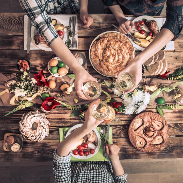 Traditional Easter celebration, Easter holiday party. Holiday friends or family at the festive table with rabbit meat, vegetables, pies, eggs, top view. Friends hands eating and drinking together.