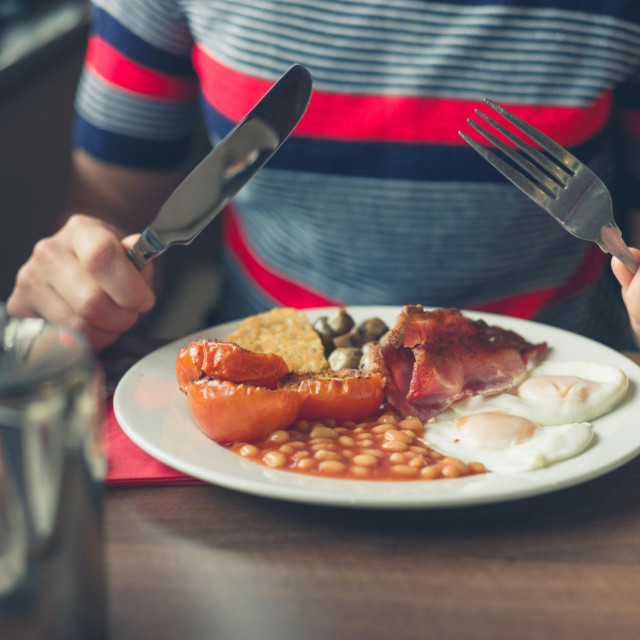 A young woman is having a traditional english breakfast in a diner