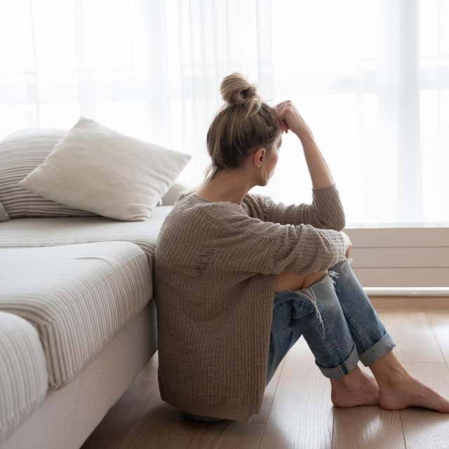 A depressed woman is sitting on the floor in the living room.