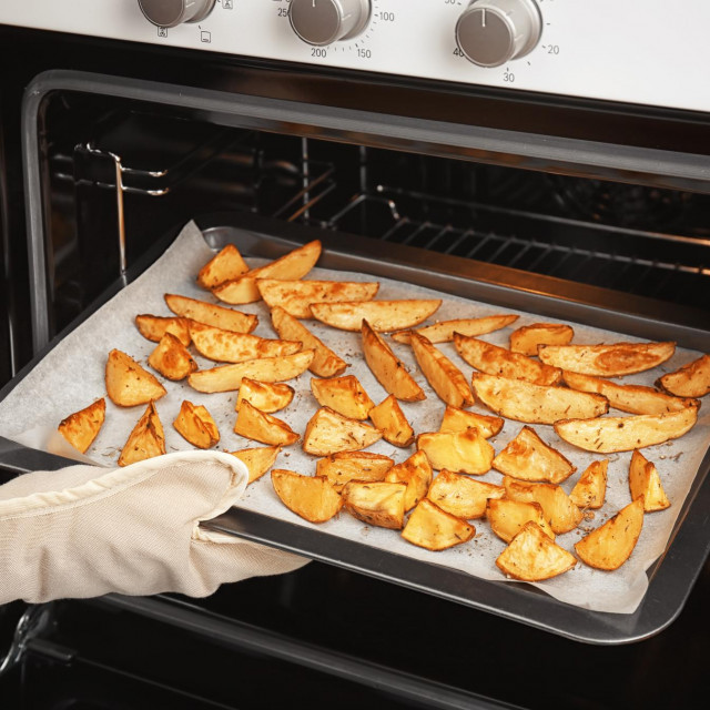 Woman taking baking sheet with delicious potatoes from oven