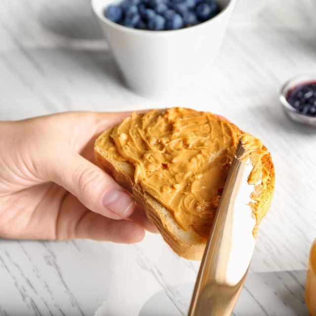 Woman spreading peanut butter on slice of bread near kitchen table