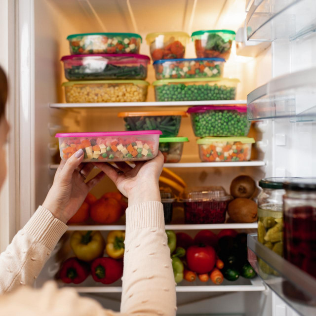Close up shot of woman taking container with frozen mixed vegetables from refrigerator while looking at camera.