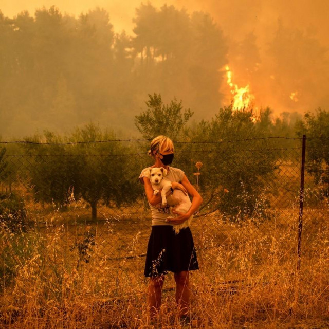 Žena drži psa u rukama dok se plamenovi vatre približavaju selu Pefki na otoku Eubeji

 