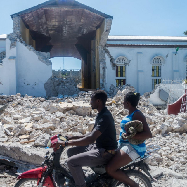 Haićani se voze pored ostataka ”Sacré coeur des Cayes” crkve u Les Cayes.
