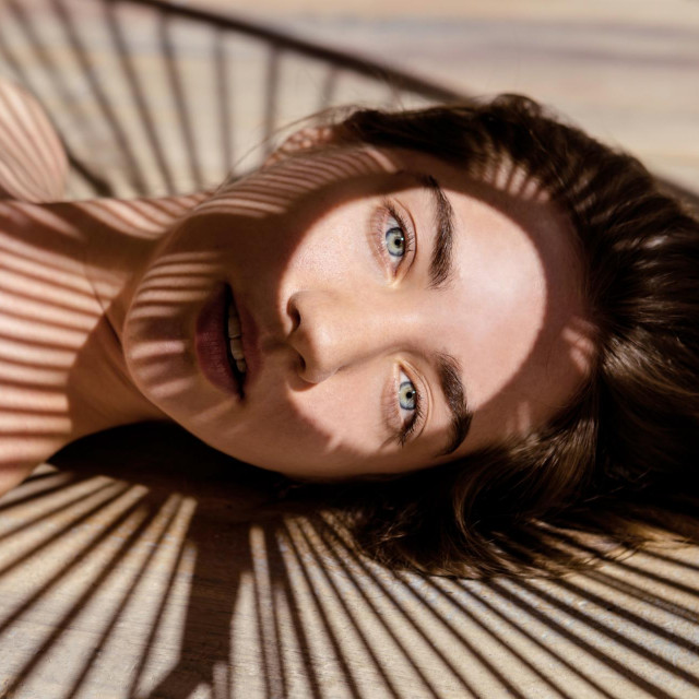 Portrait of beautiful woman with shadows of palm leaf on her face. Concept of sunbathing, vacation.
