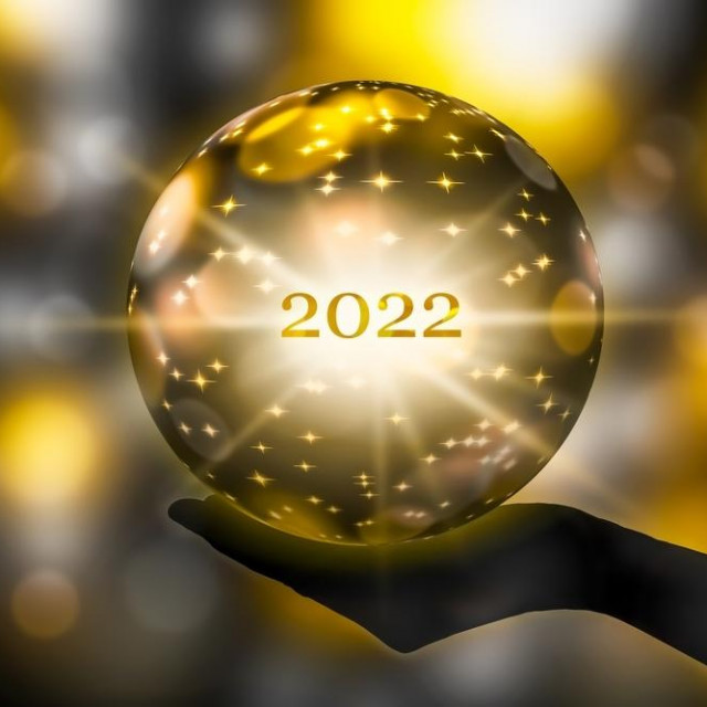 golden crystal ball in a hand, prediction for 2022, brights stars and sparks on abstract shiny background
