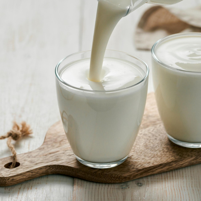 &lt;p&gt;Pouring kefir, buttermilk or yogurt with probiotics. Yogurt flowing from glass bottle on white wooden background. Probiotic cold fermented dairy milk drink. Vertical&lt;/p&gt;

