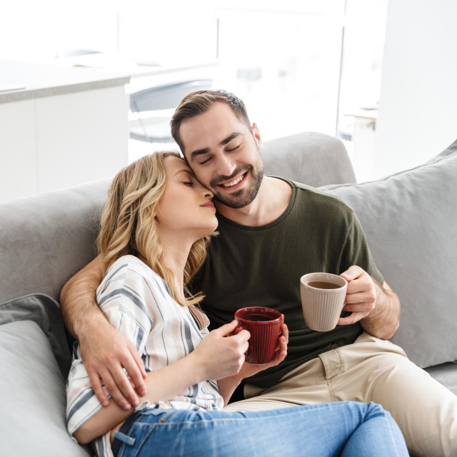 &lt;p&gt;Happy couple watching TV while sitting on a couch at the living room, drinking tea, embracing&lt;/p&gt;
