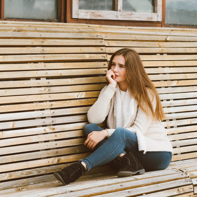 &lt;p&gt;Beautiful young girl with long brown hair sits on a wooden bench made of planks and rests, relaxes and reflects. Outdoor photo shoot with attractive woman in winter or autumn&lt;/p&gt;
