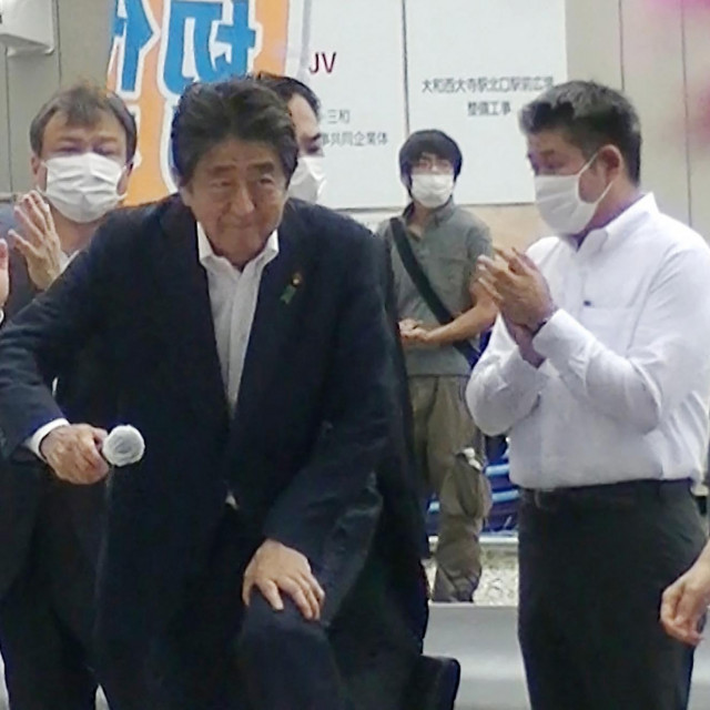 &lt;p&gt;Shinzo Abe se penje na pozornicu dok iz pozadine sve prati atentator (drugi s desne strane)&lt;/p&gt;