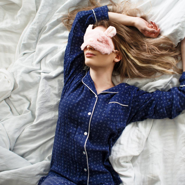 <p>Cute blonde in her bed in blue pajamas and sleep mask, top view</p>