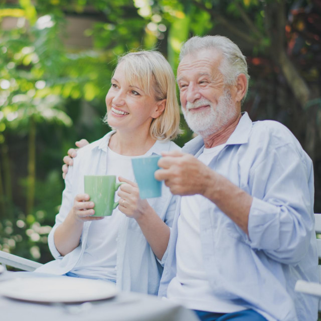<p>Closed up senior Caucasian couple talking with holding a cup of coffee on hand and felling happy in green garden. Lunch or tea time on picnic table in summer. Big family outdoor party concept.</p>