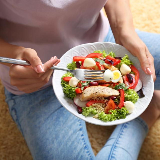 &lt;p&gt;Young woman eating tasty chicken salad with vegetables while sitting on floor&lt;/p&gt;