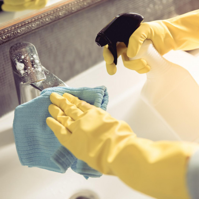 Cropped image of beautiful young woman using a duster and a detergent while cleaning sink and tap in bathroom