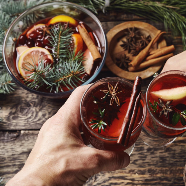 &lt;p&gt;first person view of mans and womans hands holding glasses with Christmas hot mulled red wine with spices and fruits on a wooden rustic table background with spruce snow-covered branches. Traditional&lt;/p&gt;