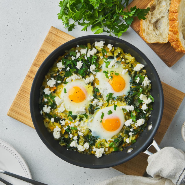 &lt;p&gt;Delicious mediterranean green shakshouka fried with eggs, spinach, celery, salty sheep milk cheese, pepper and ciabatta. Served in pan on wooden cutting board. Copy space, horizontal&lt;/p&gt;