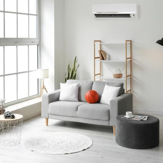 Stylish interior of light living room with sofa, shelf unit, pouf and air conditioner