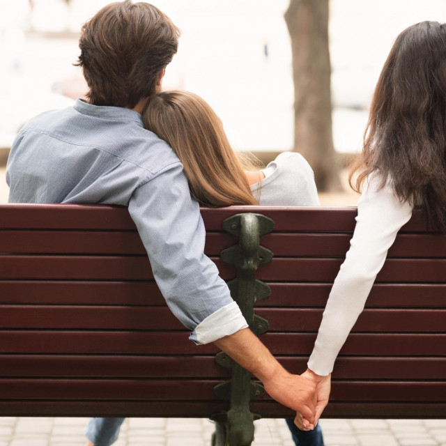 &lt;p&gt;Love Triangle. Cheating Boyfriend Hugging Girlfriend Holding Hands With Her Girl Friend Sitting On Bench Together In Park Outdoor. Back-View&lt;/p&gt;