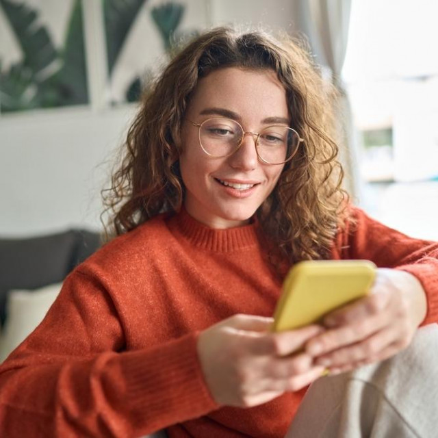 &lt;p&gt;Young smiling woman wearing glasses holding smartphone using cellphone modern technology, looking at mobile, checking cell phone apps, texting, browsing internet for shopping sitting at home.&lt;/p&gt;