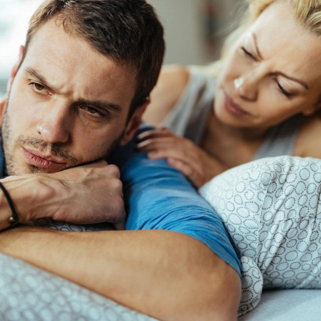 Displeased man ignoring his girlfriend while lying down in bed after the argument.