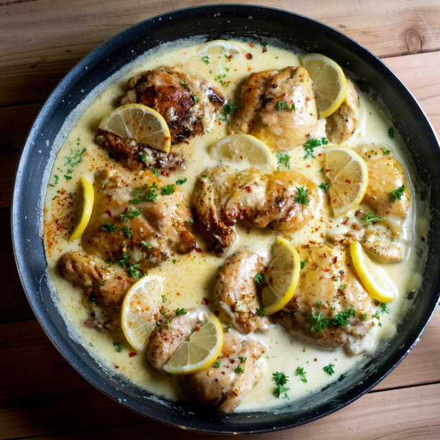 High fat, low carb lemon cream chicken seared in a pan with lemon slices and a creamy garlic sauce