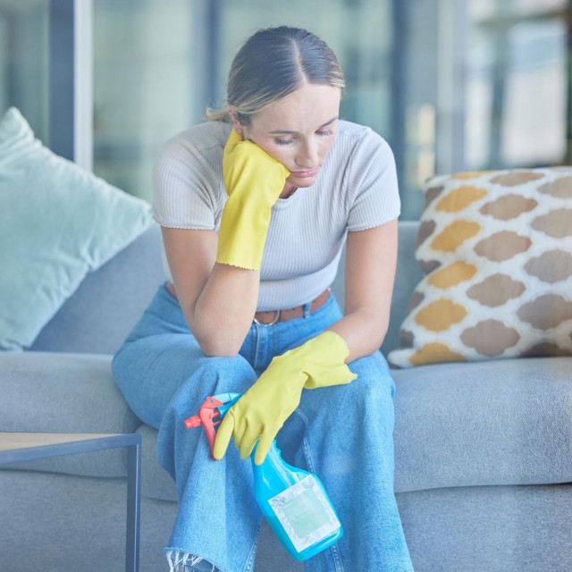 Tired, thinking and woman cleaning home on break with fatigue, unhappy and frustrated with routine. Spring cleaning, burnout and exhausted girl holding detergent spray thoughtful on lounge sofa.