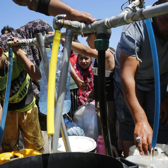 Palestinci, uključujući djecu, stoje u redu za distribuciju čiste vode putem mobilnih spremnika usred izraelskih napada