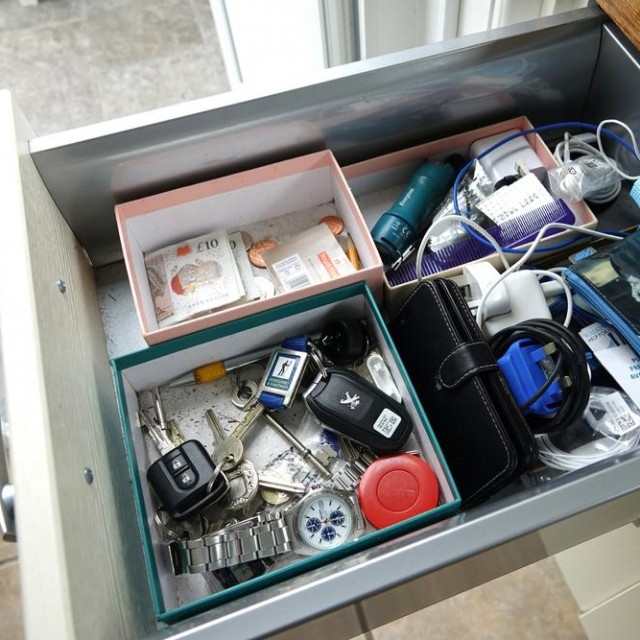 Dartmoor, England. Kitchen drawer with essential items. Car keys, mobile phone, cash and notes, postage stamps. Purse. Phone chargers, face mask. tape measure, House keys, torch, watch.