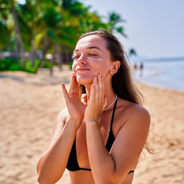 Portrait of satisfied young joyful happy smiling woman applying facial spf sunscreen while sunbathing and relaxing in the sun. Sunburn protection and healthy skin