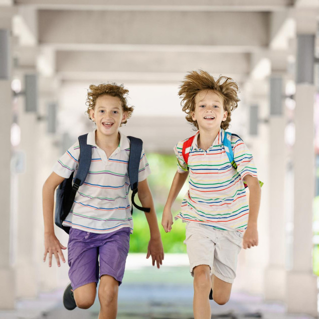 Child happy to be back to school. End or start of summer vacation for school kids. Excited happy little boy with backpack running on school yard. Student on his way home.