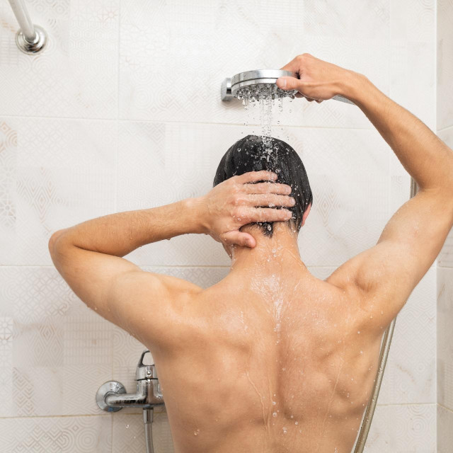 Back view of a man showering. Drops of water falling on him from the shower head