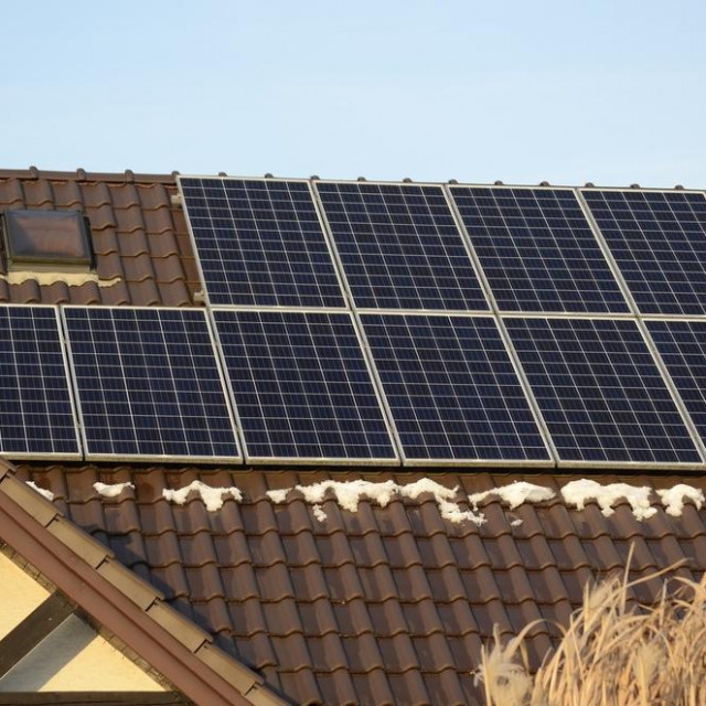 Close up photo of solar, photovoltaic panels installation on a roof of a private house in a city. Blue solar cells during winter season, some snow on panels.