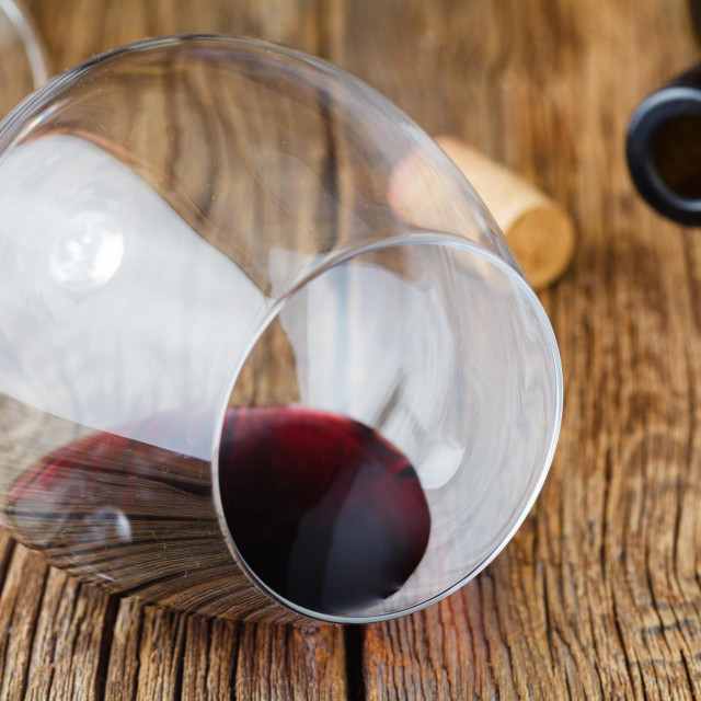 Wine glass with drop of red wine lay on table