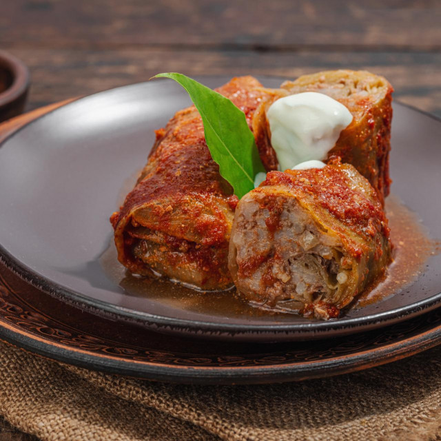 Cabbage rolls stuffed with rice and meat stewed in tomato sauce. Traditional dish, ready-to-eat food, sour cream. Old wooden background, close up