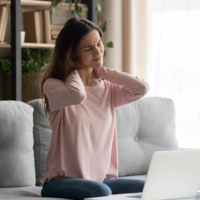 Frown woman sitting on couch near computer take break touches her neck suffers from painful feelings ache caused by poor wrong posture, sedentary work, sitting at laptop for long period concept image