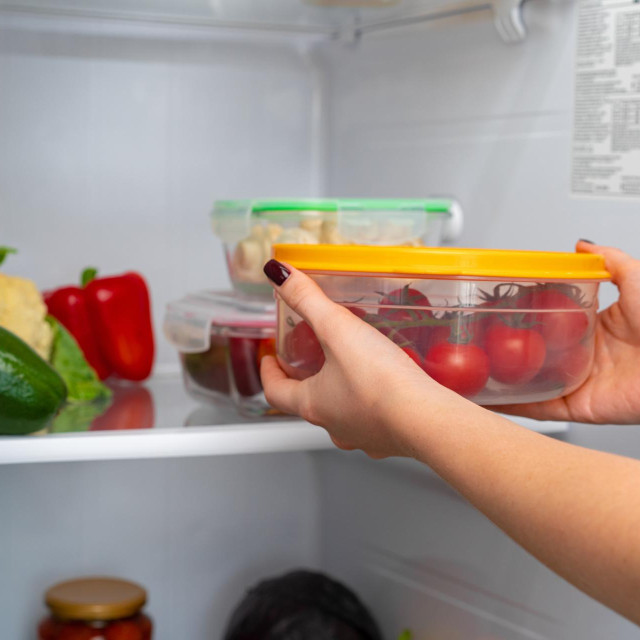 Female hands taking storage box with food from a fridge close up